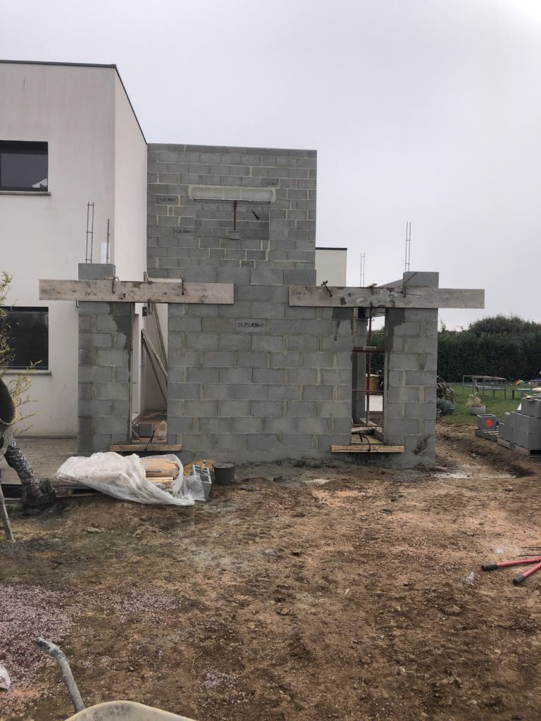 Mur en construction devant une maison moderne.